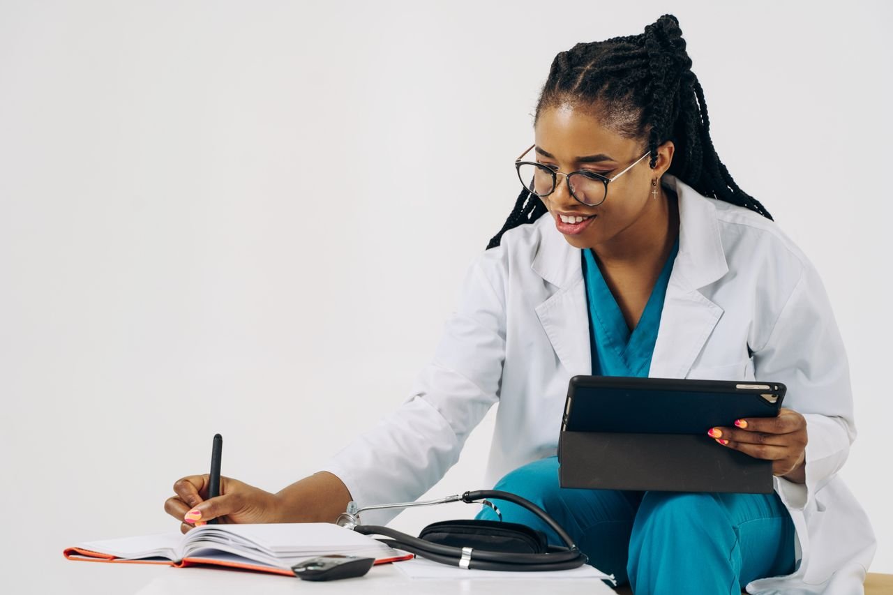 Home Smiling female doctor in scrubs using tablet and taking notes in a healthcare setting.