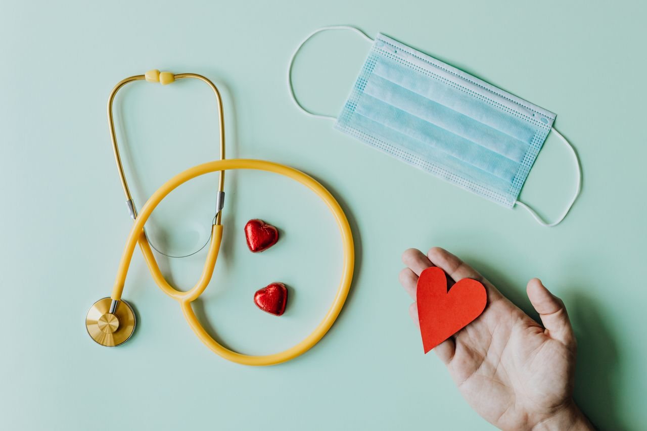 Home Top view of crop anonymous person hand with red paper heart on table with stethoscope and medical mask for coronavirus prevention